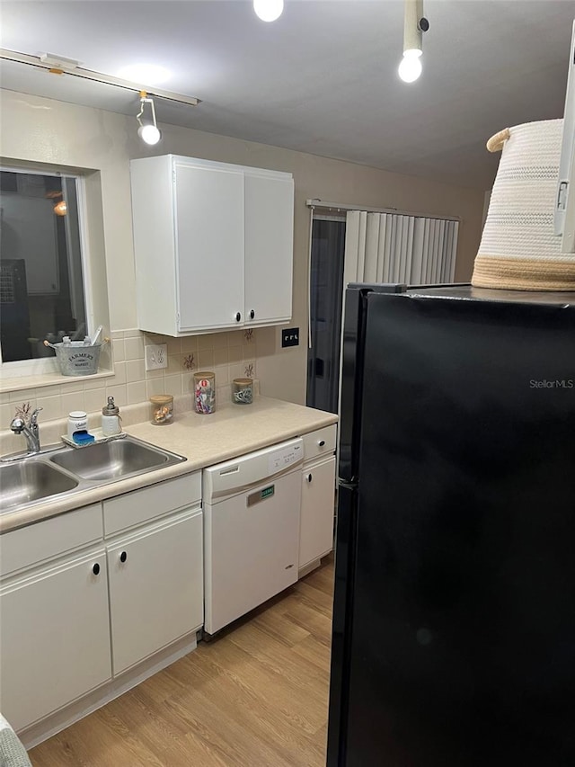 kitchen featuring white dishwasher, a sink, white cabinetry, light countertops, and freestanding refrigerator