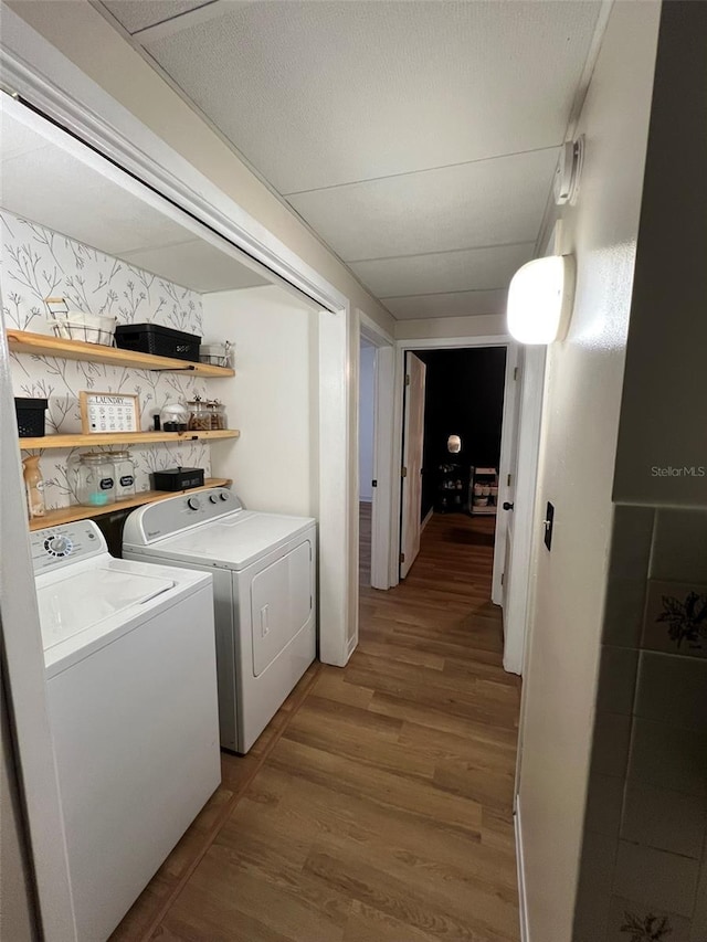 clothes washing area with a textured ceiling, laundry area, separate washer and dryer, wood finished floors, and wallpapered walls