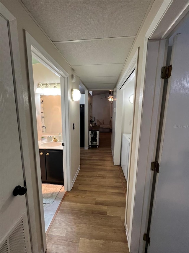 corridor featuring a textured ceiling, light wood-style flooring, a sink, visible vents, and washing machine and clothes dryer