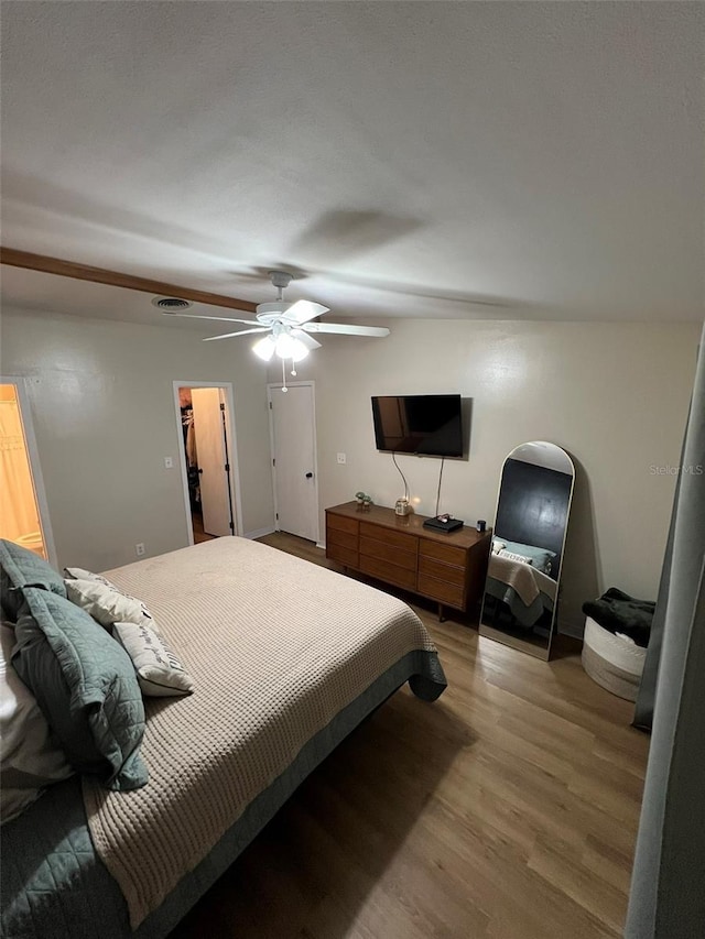 bedroom with a spacious closet, wood finished floors, visible vents, and a ceiling fan