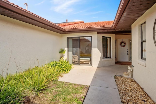 view of exterior entry with a tiled roof, a patio area, and stucco siding