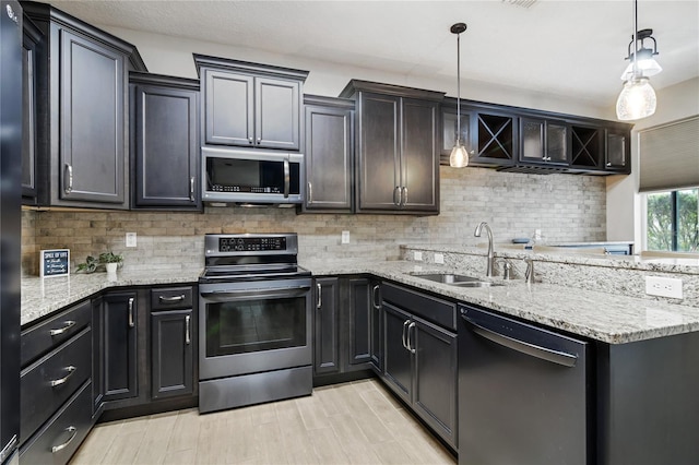 kitchen featuring light stone counters, a sink, appliances with stainless steel finishes, backsplash, and pendant lighting