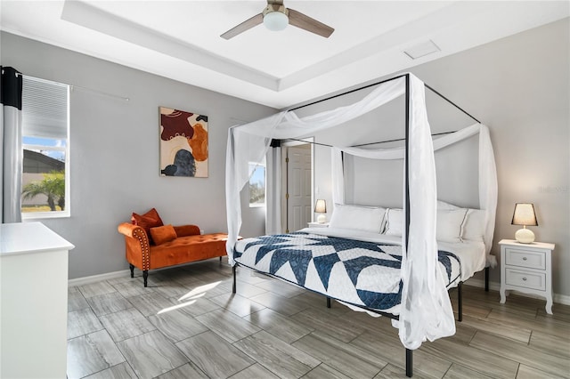 bedroom featuring a tray ceiling, wood tiled floor, a ceiling fan, and baseboards