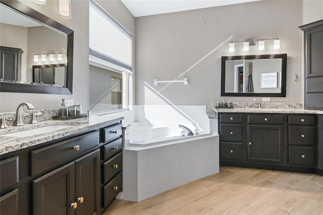 bathroom featuring two vanities, a sink, a bath, and wood finished floors