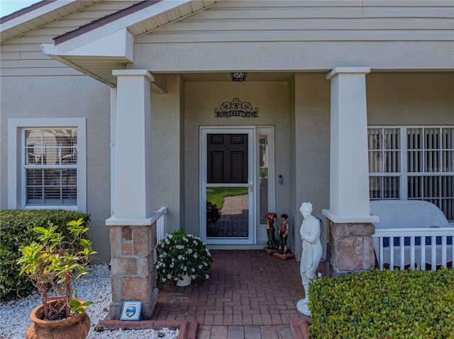 doorway to property with covered porch and stucco siding