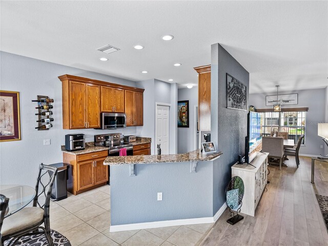 kitchen featuring light stone counters, a breakfast bar, visible vents, appliances with stainless steel finishes, and brown cabinetry