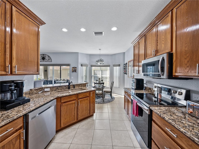 kitchen with light tile patterned floors, visible vents, brown cabinetry, appliances with stainless steel finishes, and a sink