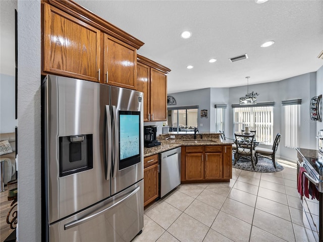 kitchen featuring light tile patterned floors, brown cabinetry, a peninsula, stainless steel appliances, and a sink