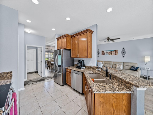 kitchen with brown cabinets, stainless steel appliances, stone countertops, a sink, and a peninsula