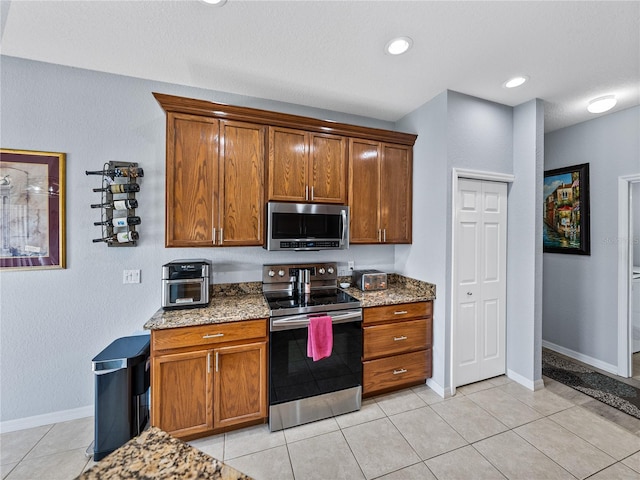 kitchen featuring baseboards, appliances with stainless steel finishes, stone countertops, and brown cabinets