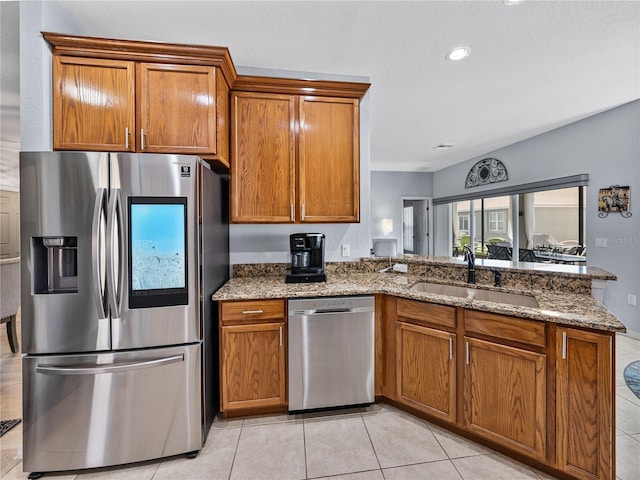 kitchen featuring brown cabinets, dark stone counters, stainless steel appliances, and a sink