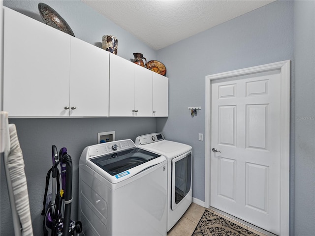 washroom with light tile patterned floors, a textured ceiling, cabinet space, and washer and dryer