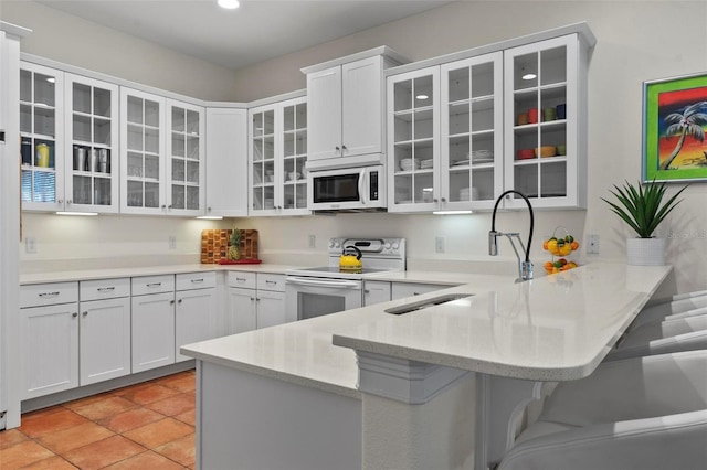 kitchen featuring a peninsula, white appliances, glass insert cabinets, and white cabinetry