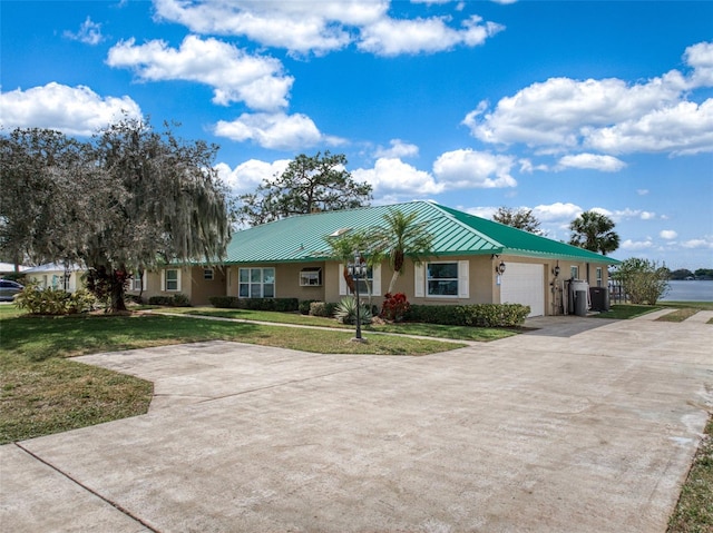 single story home with an attached garage, concrete driveway, stucco siding, a front lawn, and a standing seam roof