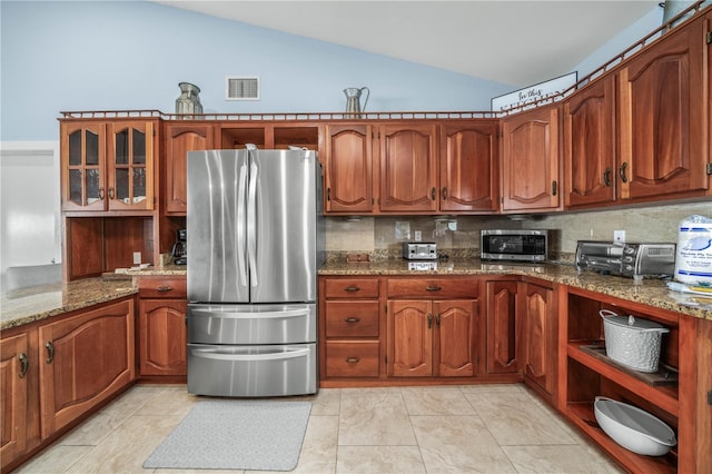 kitchen featuring a toaster, brown cabinetry, lofted ceiling, appliances with stainless steel finishes, and light stone countertops