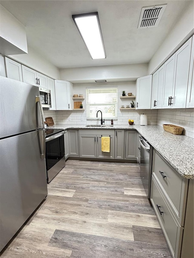 kitchen featuring light stone counters, open shelves, visible vents, appliances with stainless steel finishes, and a sink