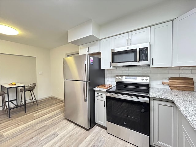 kitchen with light wood-style flooring, appliances with stainless steel finishes, white cabinets, and backsplash