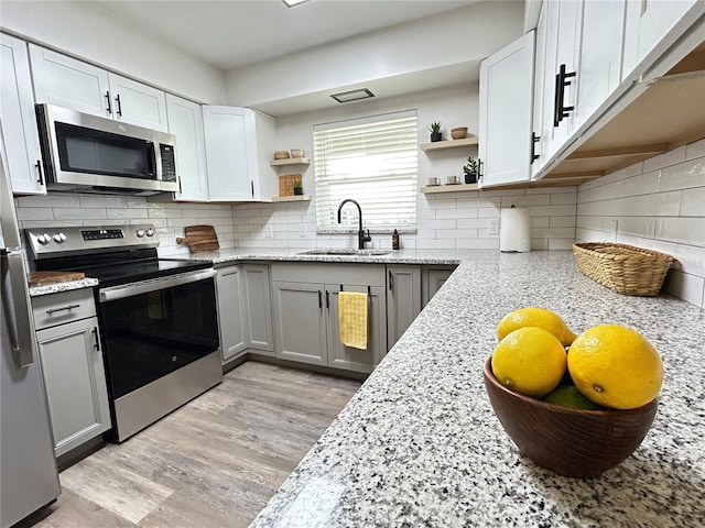 kitchen featuring white cabinets, light stone counters, stainless steel appliances, open shelves, and a sink