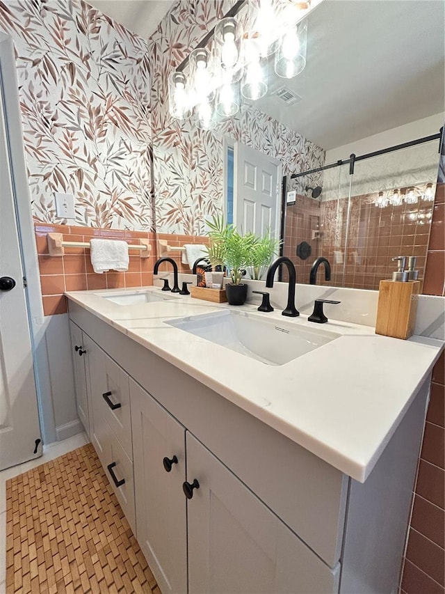 full bathroom with double vanity, wallpapered walls, walk in shower, and a sink