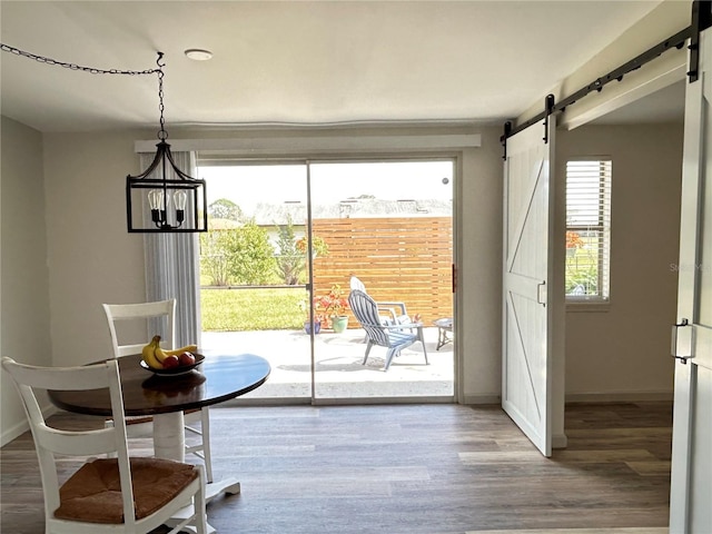 dining space featuring a notable chandelier, a barn door, baseboards, and wood finished floors