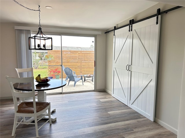 dining room featuring a chandelier, wood finished floors, baseboards, and a barn door