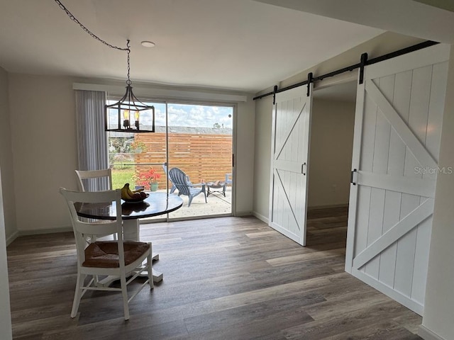 unfurnished dining area featuring a notable chandelier, a barn door, wood finished floors, and baseboards