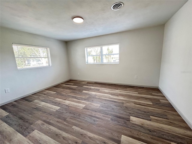 spare room with dark wood finished floors, visible vents, and baseboards