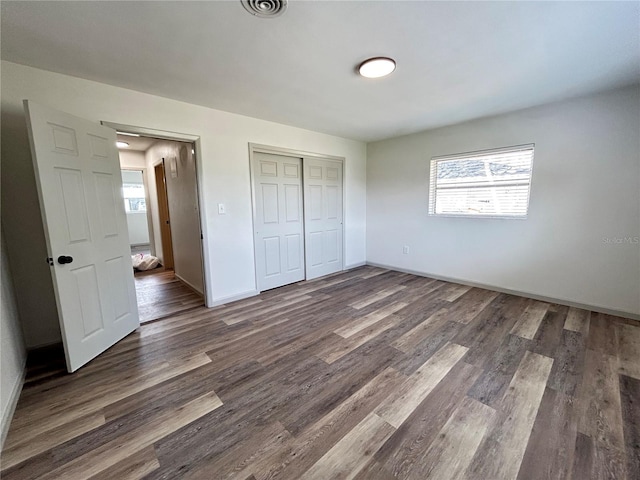 unfurnished bedroom featuring baseboards, a closet, visible vents, and dark wood-style flooring