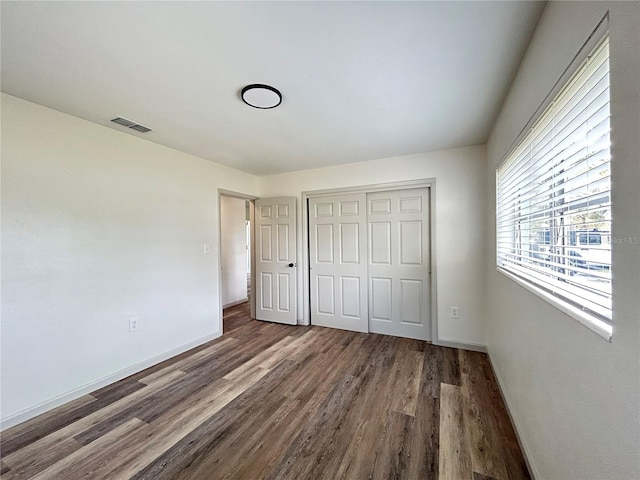 unfurnished bedroom with a closet, dark wood-style flooring, visible vents, and baseboards