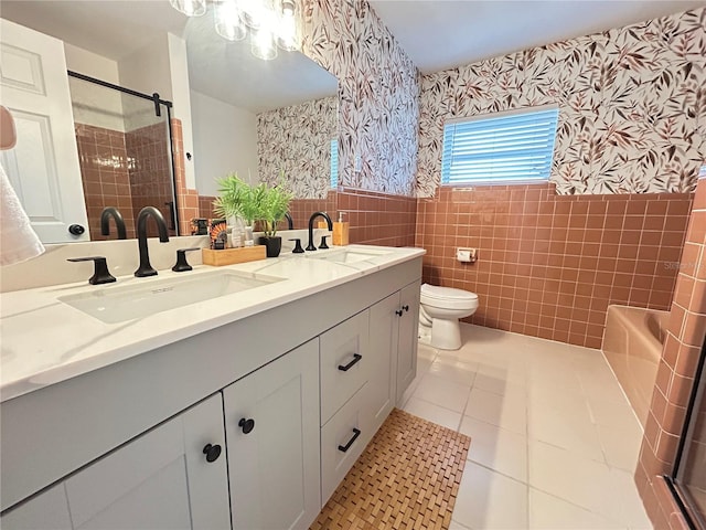 bathroom featuring wainscoting, a sink, tile walls, and wallpapered walls