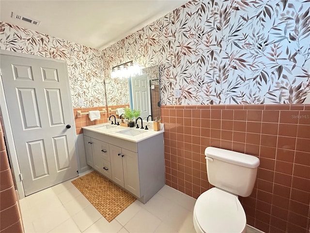 bathroom with a wainscoted wall, visible vents, toilet, a sink, and wallpapered walls