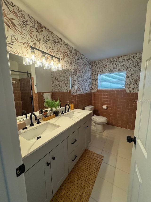 full bath featuring wainscoting, a sink, tile walls, and wallpapered walls