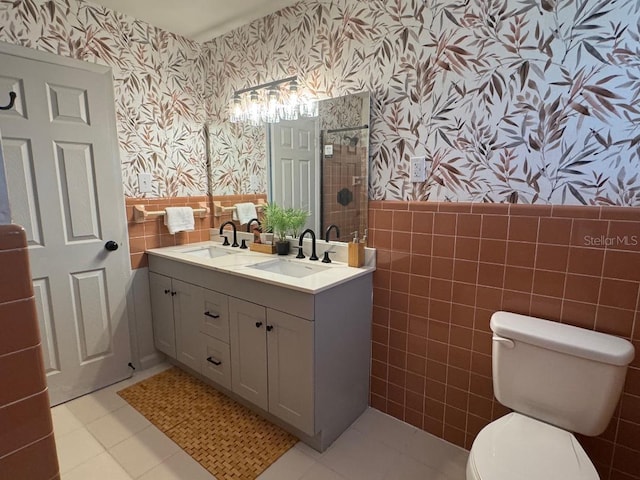 bathroom featuring a wainscoted wall, a sink, tile walls, and wallpapered walls