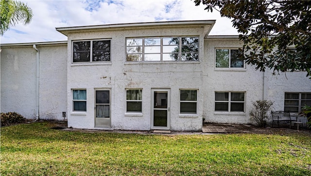 back of house with a lawn and stucco siding