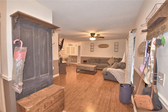 living room with a textured ceiling, wood finished floors, a ceiling fan, and baseboards