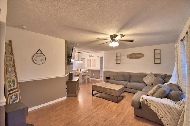 living room featuring baseboards, a textured ceiling, a ceiling fan, and wood finished floors