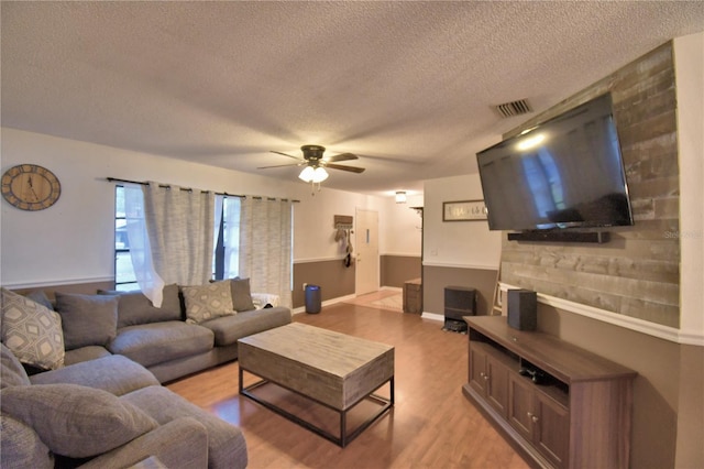 living room featuring light wood-type flooring, visible vents, ceiling fan, and a textured ceiling