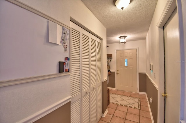 doorway to outside with light tile patterned flooring, a textured ceiling, and baseboards