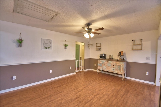 unfurnished room featuring a textured ceiling, wood finished floors, a ceiling fan, and baseboards