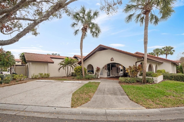 mediterranean / spanish house with a front yard, a tile roof, uncovered parking, and stucco siding