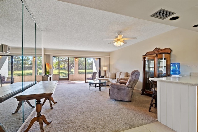 living room featuring a textured ceiling, a ceiling fan, visible vents, and light colored carpet