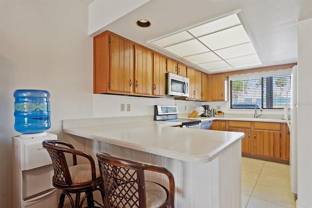 kitchen with stainless steel appliances, brown cabinetry, a peninsula, and light countertops