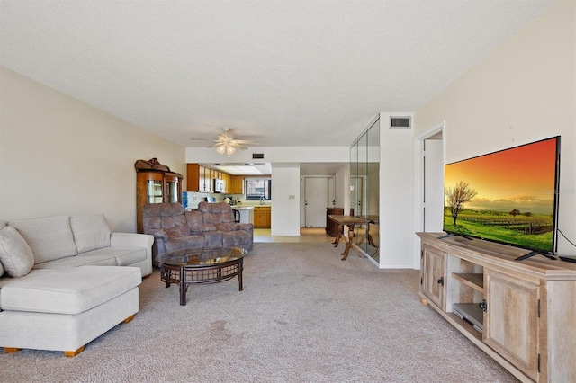 living room featuring light carpet, ceiling fan, visible vents, and a textured ceiling