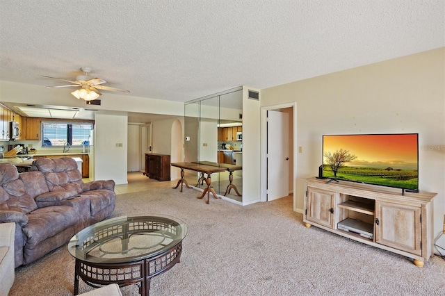 carpeted living room with arched walkways, visible vents, a textured ceiling, and a ceiling fan