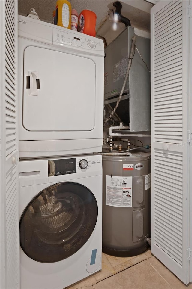 clothes washing area featuring laundry area, electric water heater, stacked washing maching and dryer, and light tile patterned floors