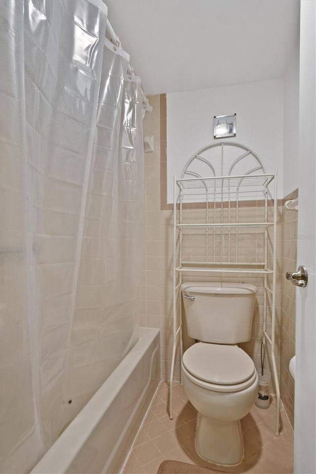 bathroom featuring tile patterned flooring, shower / bathtub combination with curtain, tile walls, and toilet