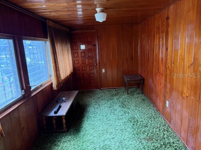 interior space featuring wooden ceiling, carpet flooring, and wooden walls