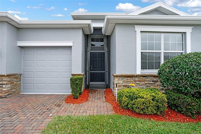 view of exterior entry with a garage, stone siding, decorative driveway, and stucco siding