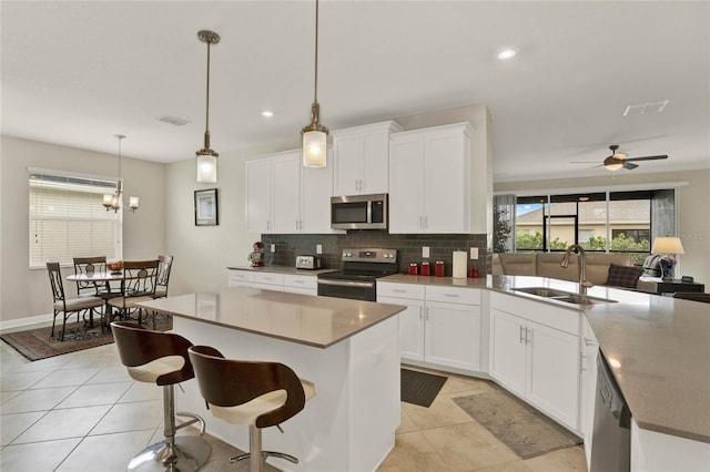 kitchen with appliances with stainless steel finishes, white cabinets, a kitchen island with sink, and a sink