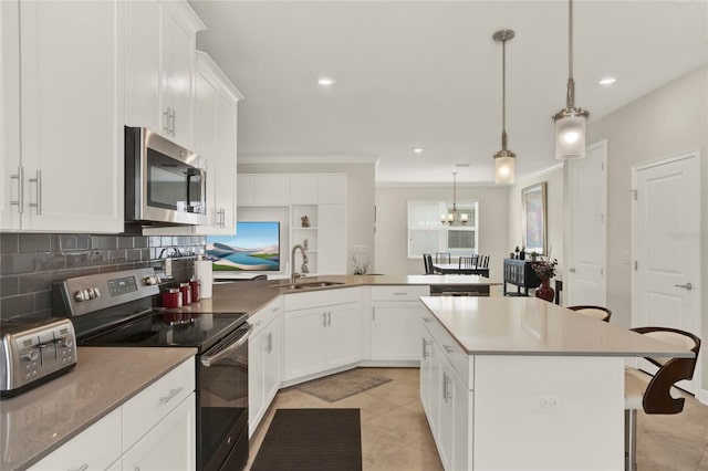 kitchen with a peninsula, a sink, a kitchen breakfast bar, appliances with stainless steel finishes, and decorative light fixtures